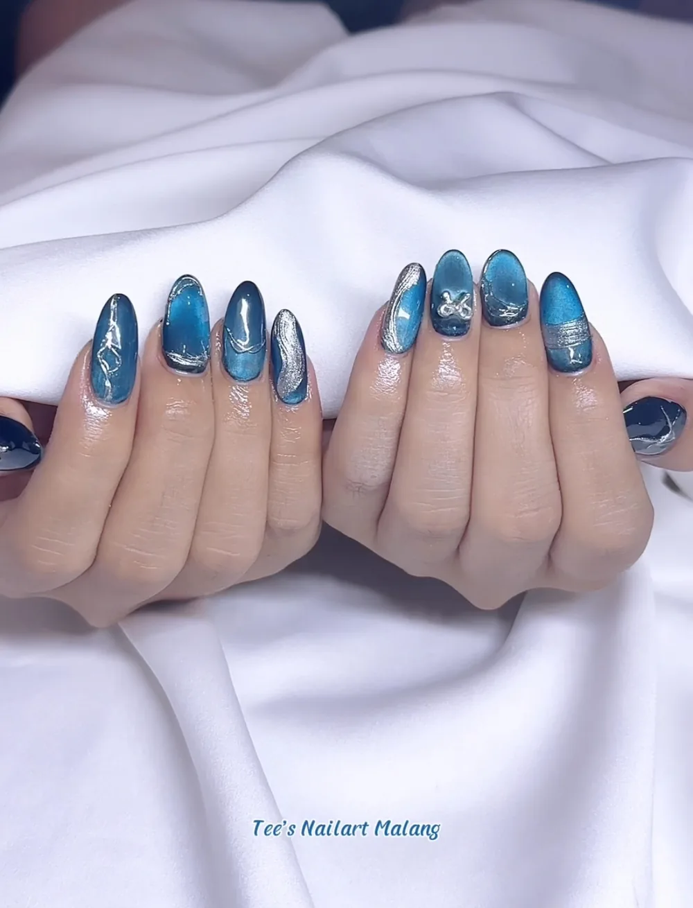 Blue cat-eye nails with silver chrome and abstract swirl details
